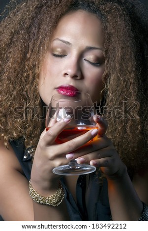 Beautiful brunette woman with curl hair feels red wine aroma emanating holding the cup in his hands