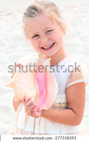 little girl with white hair smiles and holds a sea shell