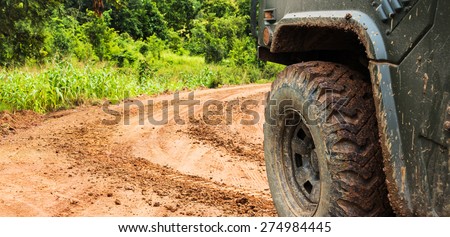 The wheels of car go round on dirt road.