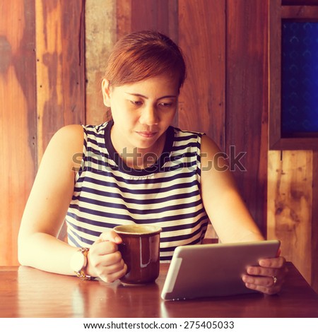 Asian woman using tablet computer in cafe drinking coffee. Focus on her face. (Vintage process tone)