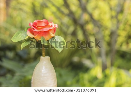 Artificial roses in a white vase against blurry nature background