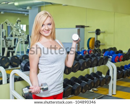 Beautiful happy young woman exercising with free weights in gym