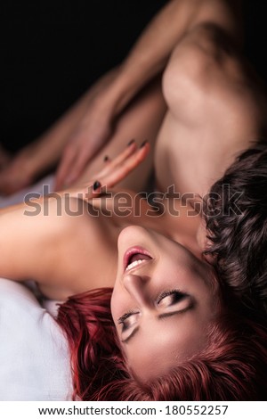 Young beautiful amorous couple making love in bed on a dark background