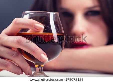 Woman in depression, drinking alcohol. Focus on glass