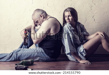 Young couple in the fight against alcoholism sitting on the floor of an empty room