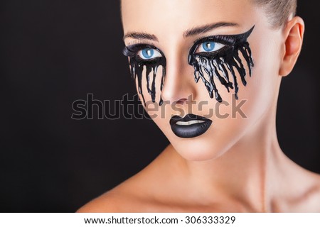Closeup of a beautiful woman with fantasy makeup with black tears and lips on a black background