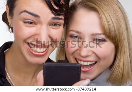 Two laughing women in close up look at mobile phone on light background