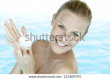 Smiling woman applying cream on her face. Woman in swimming pool.