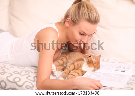young woman lying on a sofa with her cat and reading a book