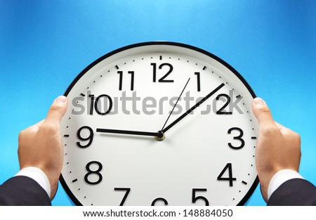 Time management. Businessman holding a wall clock.