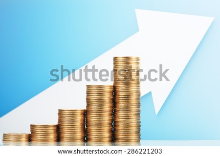Pile of coins and growing arrow. Earning and saving more money. Pile of 500 yen coins with upside growing arrow. Blue reflection background.
