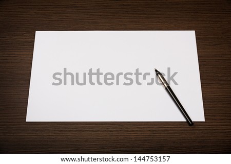 Blank sheet of paper and pen on dark wooden office desk.