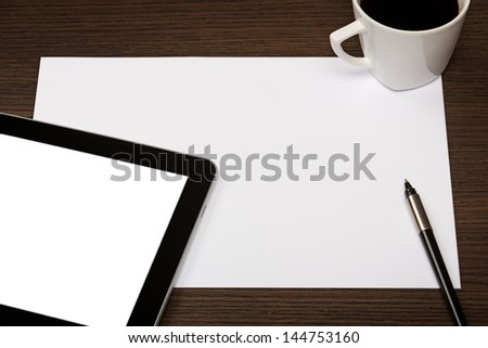 Digital tablet with blank screen, sheet of paper, pen and cup of coffee on dark wooden office desk.