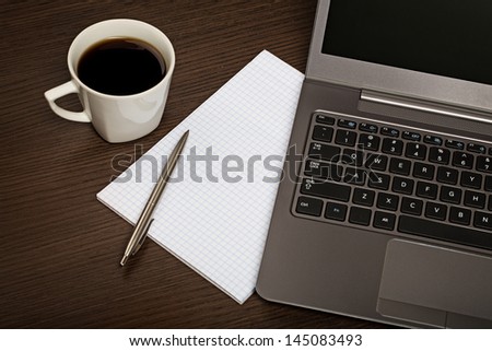 Top view on dark wooden office desk with sheet of paper, pen, laptop and cup of coffee.