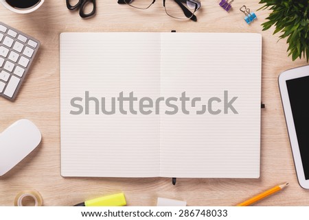 Opened notebook and other office equipment such as computer keyboard, mouse, digital tablet, pencil, mug of coffee and glasses on wooden office desk.