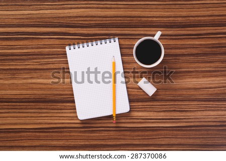 Notepad, pencil and mug of black coffee on dark wooden office desk.