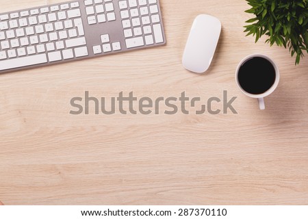 Modern computer keyboard, white mouse, mug of coffee and green plant on bright wooden office desk.