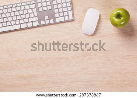 Empty space next to office equipment such as computer modern keyboard, white mouse and green apple on bright wooden office desk.