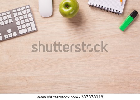 Empty space next to office equipment such as computer modern keyboard, white mouse, notepad, pencil, green apple and highlighter on bright wooden office desk.