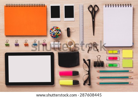 Digital tablet, photos, calendar, notepad, wallet, clips, glasses and other office equipment arranged in perfect order on bright wooden office desk.