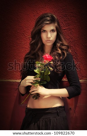 Beautiful girl with red rose near textured wall