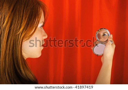Girl holding and looking in the mirror, with theater curtain in background. Focus is on the mirror