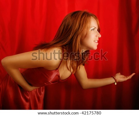 Side half body portrait of young woman taking bow on stage with red curtains in background.