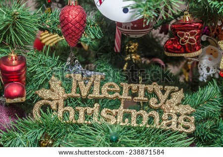 Detail of green Christmas (Chrismas) tree with Merry Christmas write, colored lights, globes, stars, Santa Claus, Snowman, shoes, candles, bells, white transparent angels, snow flakes and candy sticks