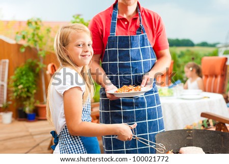 Happy family having a barbecue in summer; the father and a child standing at the grill