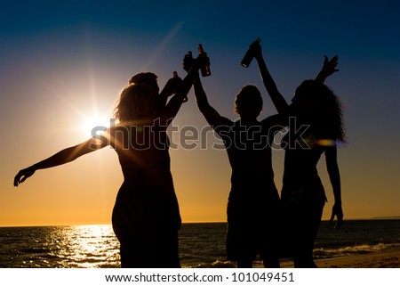 People (two couples) on the beach having a party, drinking and having a lot of fun in the sunset (only silhouette of seen, people having bottles in their hands with the sun shining through)
