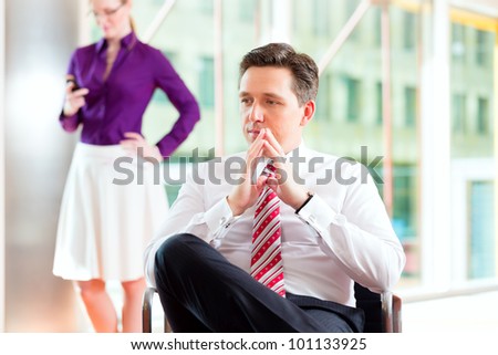 Business people - boss and secretary in office, he is sitting and she makes a phone call