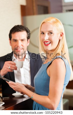 Working colleagues - a man and a woman - sitting in cafe working and drinking coffee