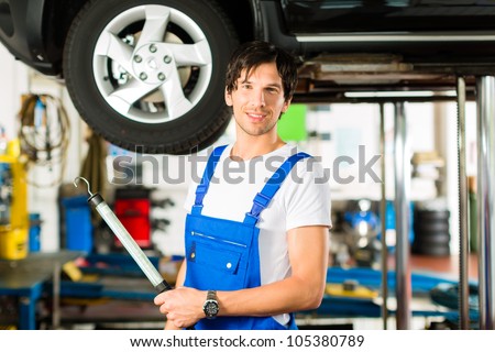 Young man in blue overall - mechanic - working with lamp on jacked car in a service station