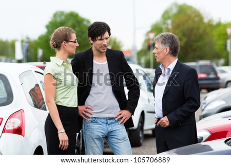 Mature car dealer and young couple standing on parking place at dealership in front of cars
