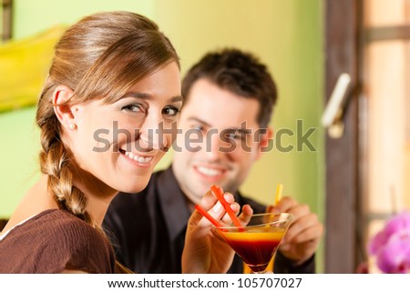 Young happy couple drinking cocktails in bar or restaurant; presumably it is a first date