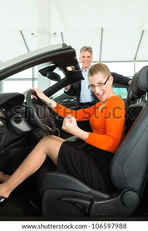 Young woman with mature man sits in car on driver seat with her hand on the steering wheel in a car dealership, obviously she is buying or selling the convertible