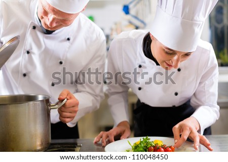 Two chefs - man and woman - in hotel or restaurant kitchen working and cooking in team