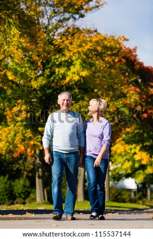 Man and woman, senior couple, having a walk in autumn or fall outdoors, the trees show colorful foliage
