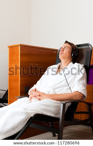 Young man relaxing in spa hearing music with headset in quiet room
