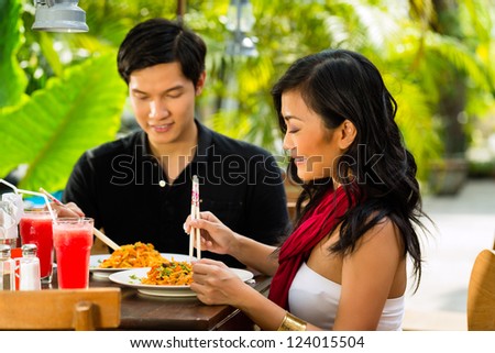 Asian man and woman in restaurant eating their food with chopsticks