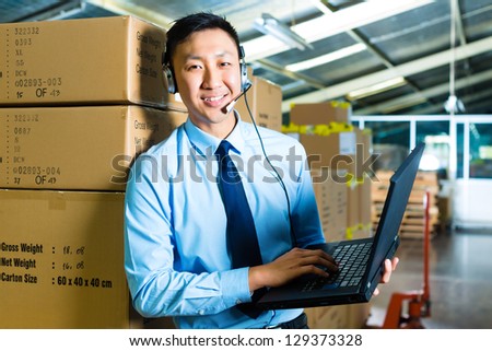 Young man in a suit with headset and laptop in a warehouse, he is from the Customer Service