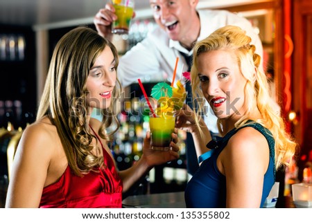 Young women with cocktails in bar or club, the bartender is mixing drinks