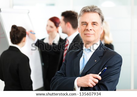 Business - team in an office, the senior executive is standing in front