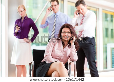 Business people - female boss and employees in office, all making a call with their mobiles