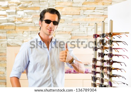 Young man at optician with glasses, he might be customer or salesperson and is looking for sunglasses