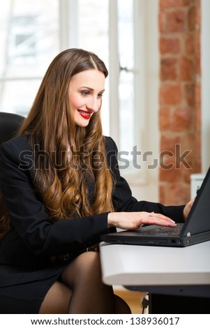 Young female businesswoman or secretary working in her office and writing on a laptop
