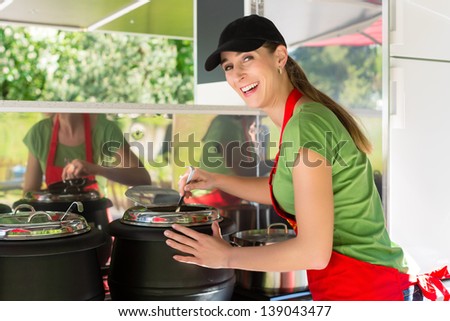 Female owner of a soup kitchen or a field kitchen stirs with a ladle in the soup