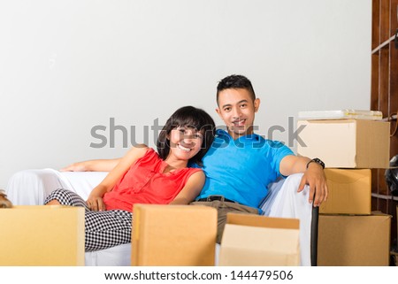 Real estate market - Young Indonesian couple moving in a home or apartment, they are sitting on the sofa and having a break