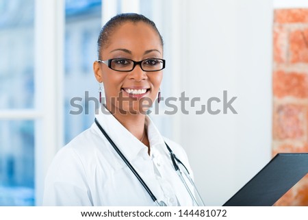 Young female black doctor standing at a window in clinic with a file or dossier