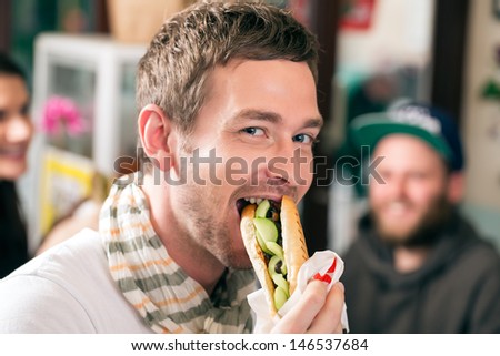 Hotdog - young customer in a snack bar eating delicious fast food sausages